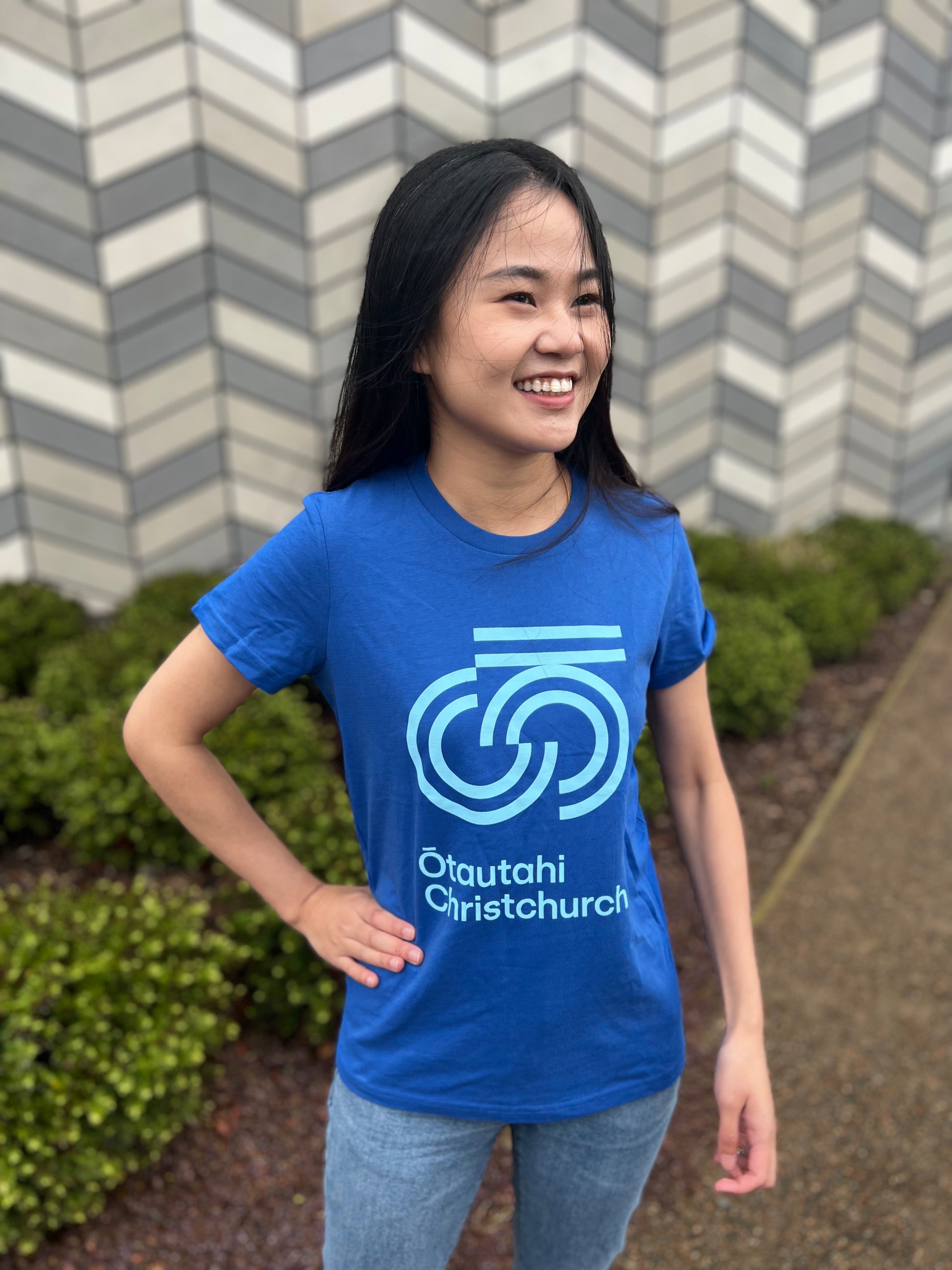 A woman wearing a blue crew neck t-shirt with text graphic on the front, standing outdoors.