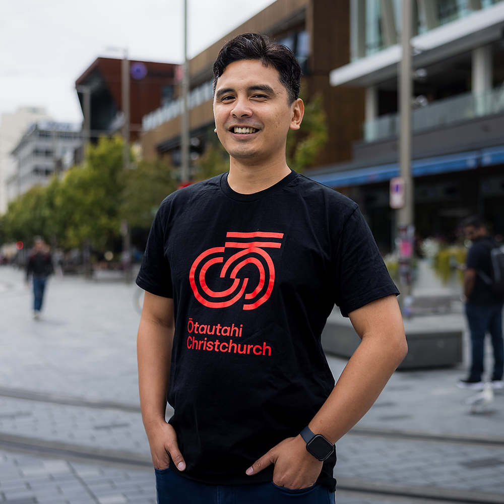 Man wearing a black t-shirt with red logo and text in an urban setting