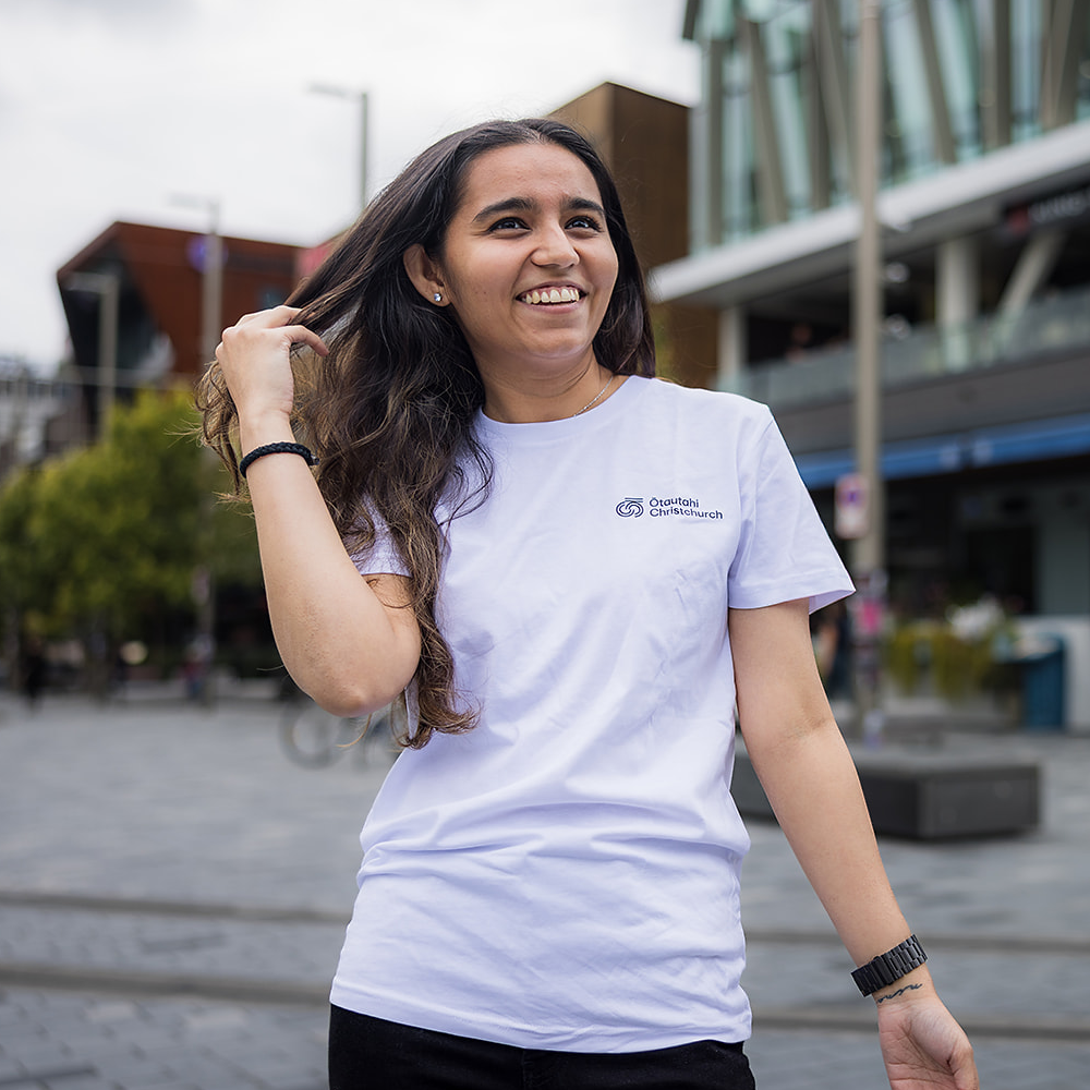 Woman wearing a white t-shirt with a logo, standing outdoors.