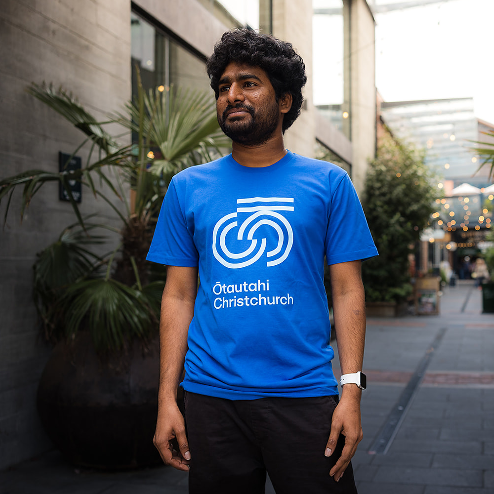 Man wearing a blue t-shirt with a logo and text, standing outdoors.