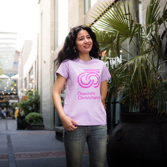 Person wearing a pink t-shirt with a logo and text, standing outdoors.